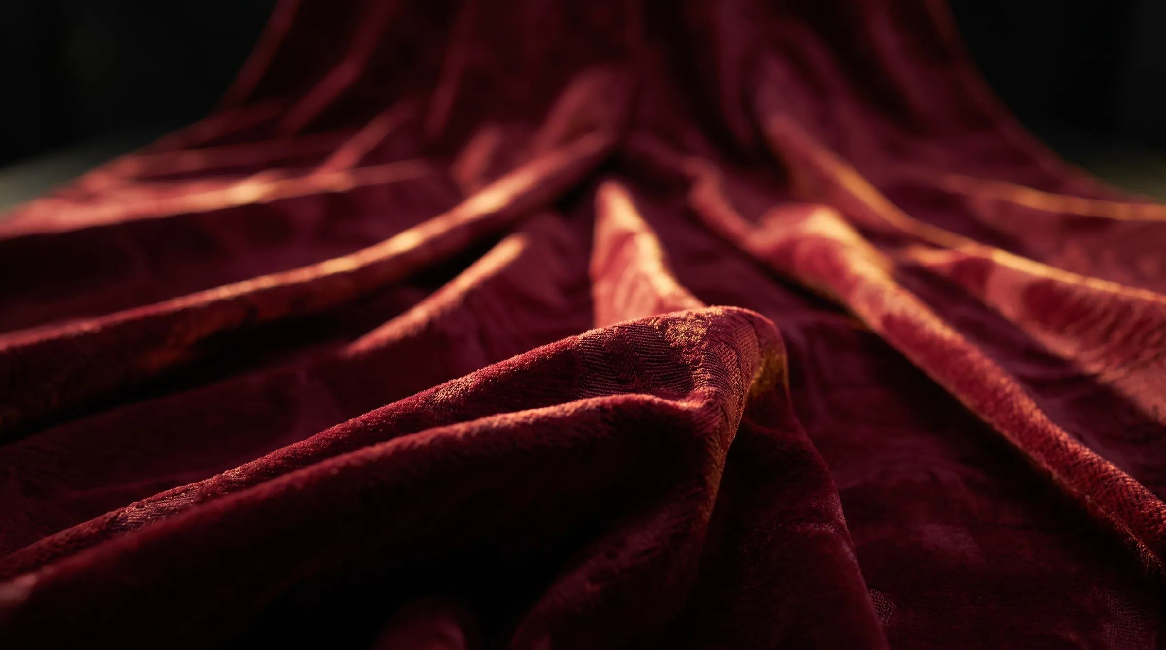 Deep crimson upholstery fabric draped under directional light, showing the weave and sheen of the material